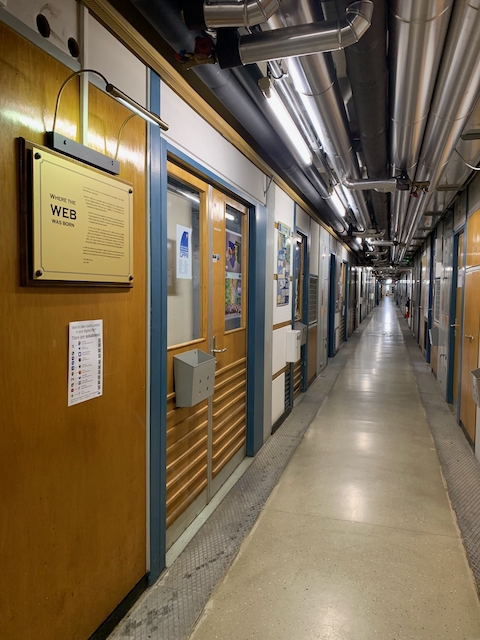 un long couloir avec des tuyaux au plafond et sur la gauche, une plaque indiquant "where the web was born"
